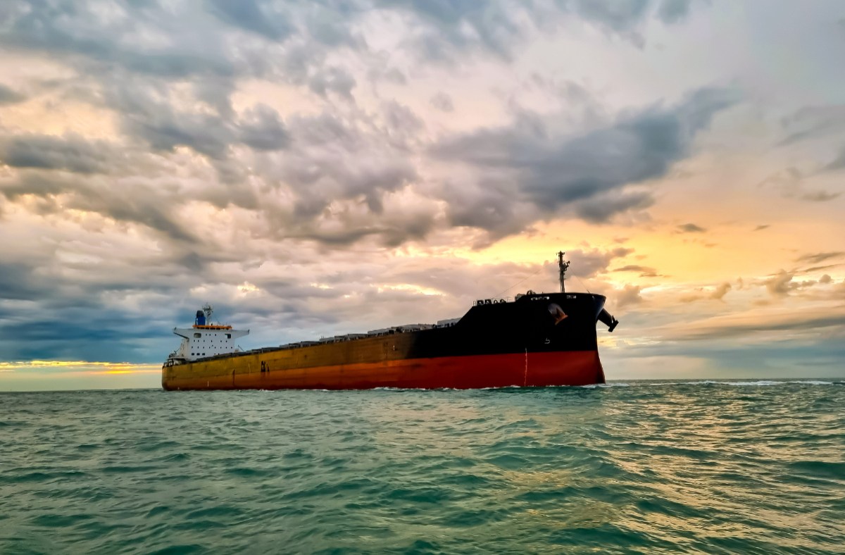 Large oil tanker navigating a strait under a cloudy sky, impacting oil prices and global trade.