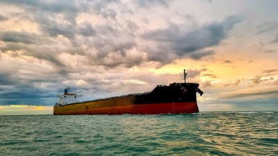 Large oil tanker navigating a strait under a cloudy sky, impacting oil prices and global trade.