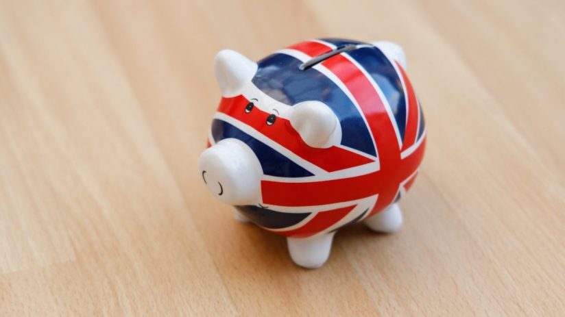 Piggy bank with Union Jack flag design on light wooden surface, symbolizing UK savings or economy.