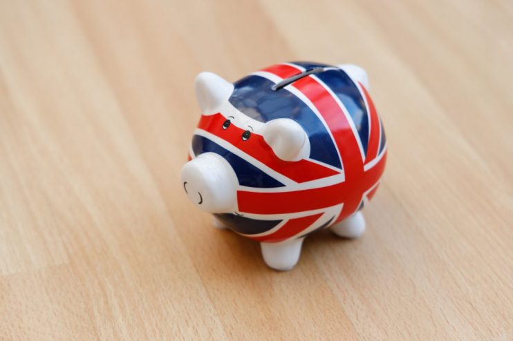 Piggy bank with Union Jack flag design on light wooden surface, symbolizing UK savings or economy.