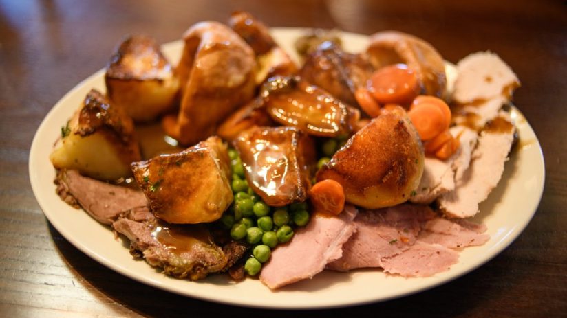 Close-up of a plated roast dinner with meat, roasted potatoes, peas, carrots, and gravy on a white plate