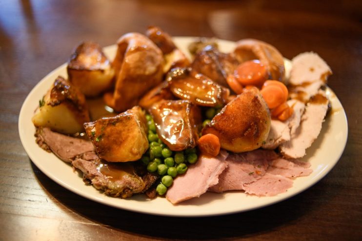 Close-up of a plated roast dinner with meat, roasted potatoes, peas, carrots, and gravy on a white plate