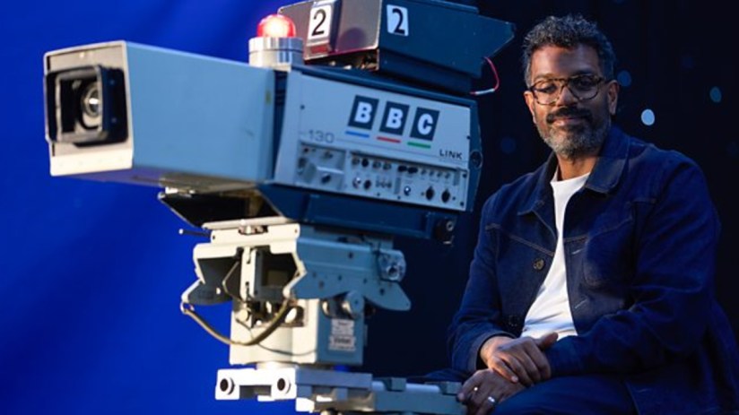 Comedian Romesh Ranganathan, smiling slightly, in a studio setting.