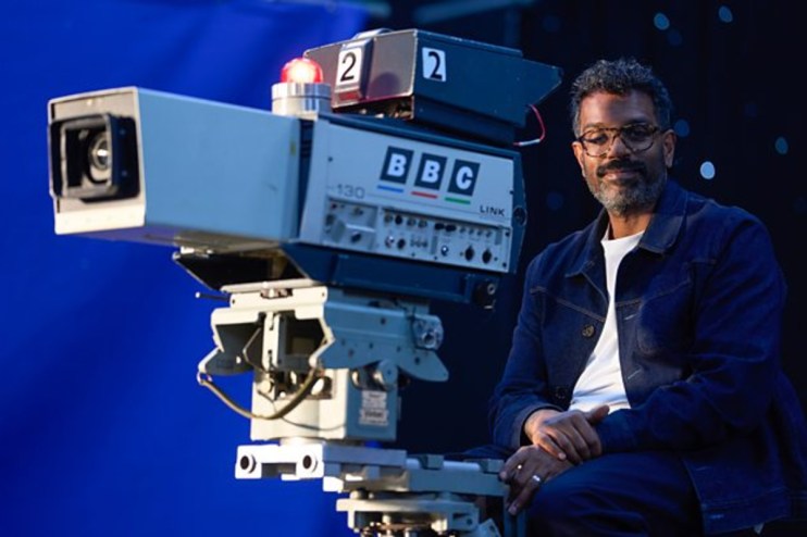 Comedian Romesh Ranganathan, smiling slightly, in a studio setting.