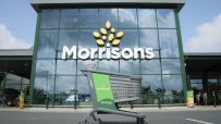 Green Instacart shopping cart outside a modern Morrisons supermarket entrance with large glass windows
