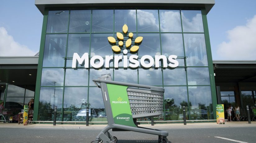 Green Instacart shopping cart outside a modern Morrisons supermarket entrance with large glass windows