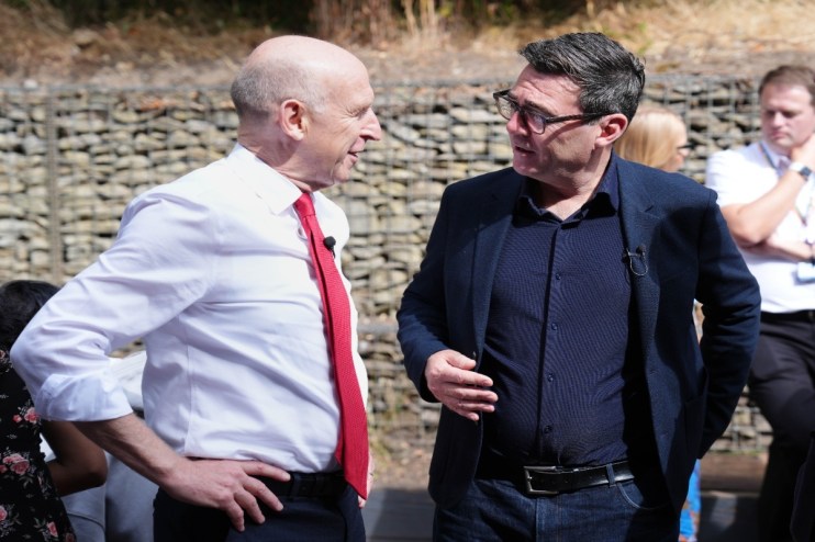 Two men, one in a white shirt and red tie, the other in a navy jacket, conversing outdoors.