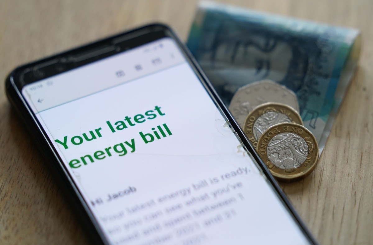 Smartphone displaying an energy bill, with British pounds and coins beside it, symbolizing rising costs.