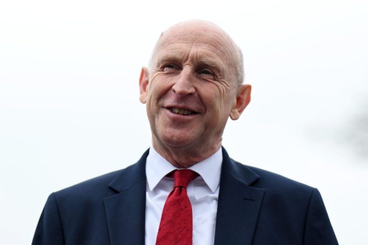 A smiling man in a dark suit and red tie looking slightly upwards, against a plain background.