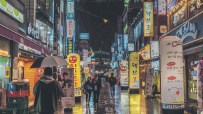 Rainy night street in Seoul, South Korea, with neon signs, storefronts, and people with umbrellas