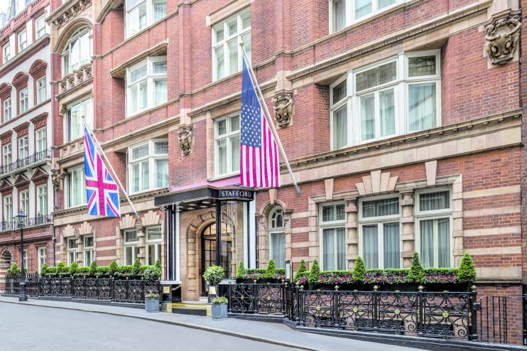 Exterior of The Stafford London hotel, a brick building with British and American flags, elegant windows, and ornate raili...