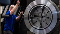 Technician in blue shirt operating a large metal lathe machine, industrial manufacturing process
