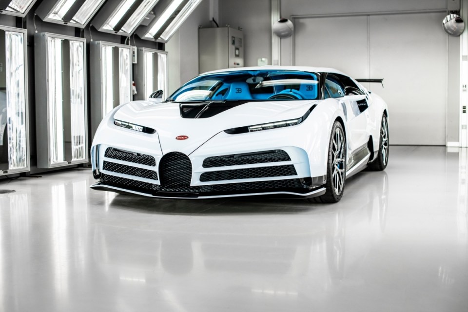 White Bugatti Centodieci hypercar with blue interior in a brightly lit showroom or factory setting.
