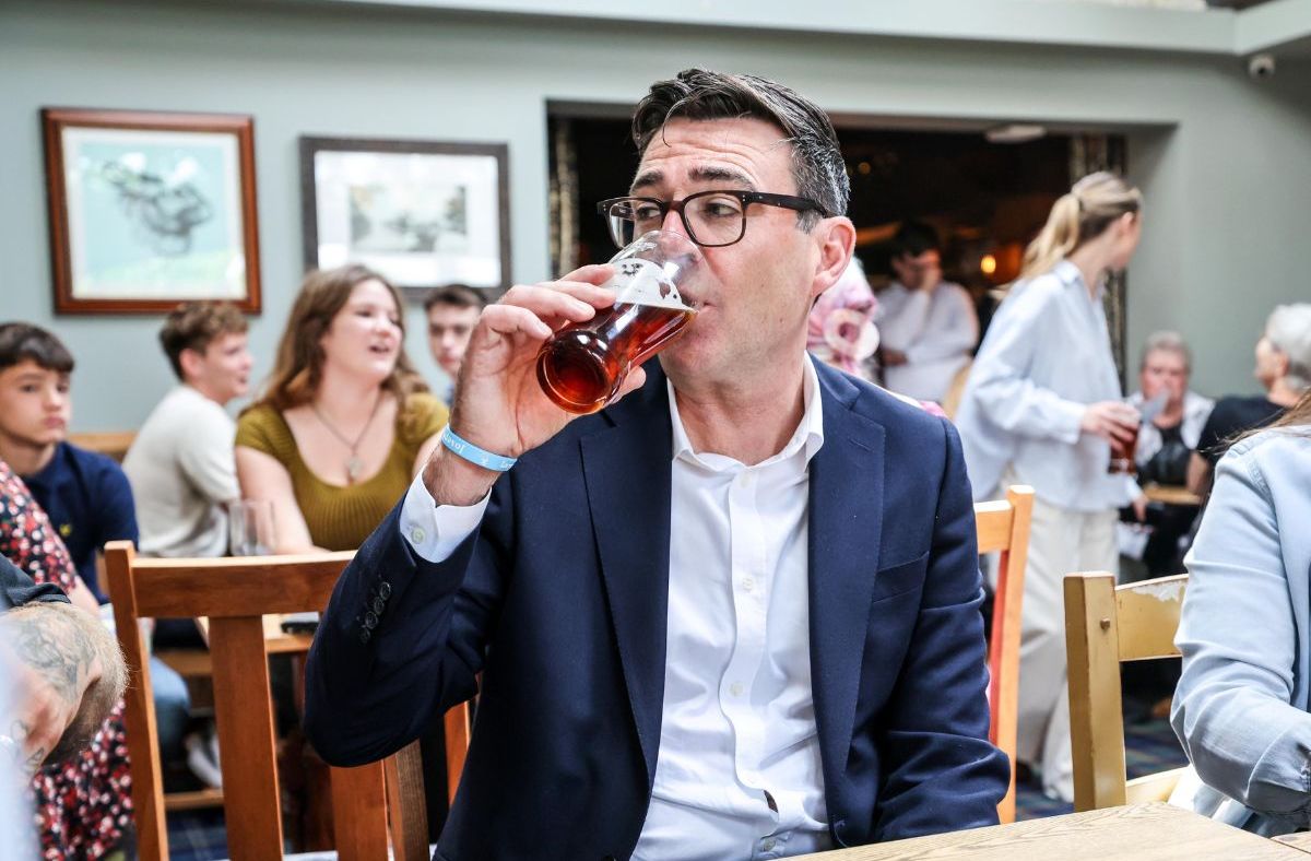 Andy Burnham in glasses drinking a pint of beer at a pub gathering.