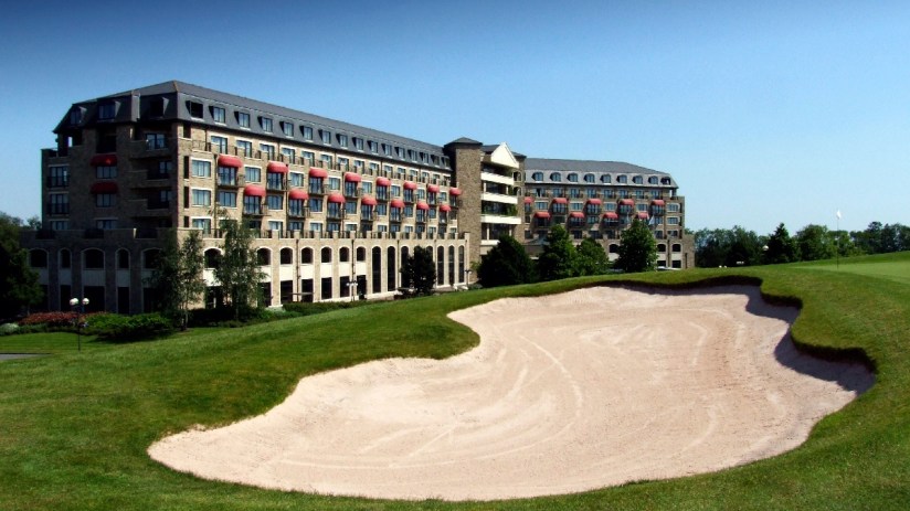 The Celtic Manor Resort in Newport, with a golf course bunker and green foreground under a clear sky.