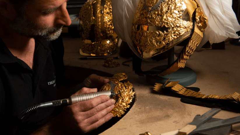Thomas Lyte designer polishing intricate gold ceremonial helmet detail with a rotary tool.