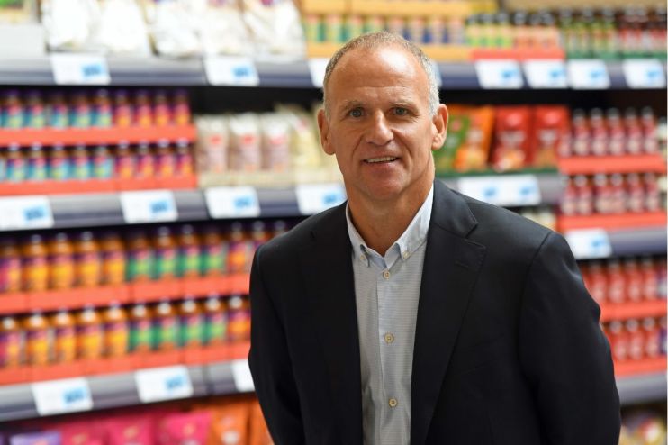 Dave Lewis, former Tesco CEO, smiling in a supermarket aisle with products on shelves
