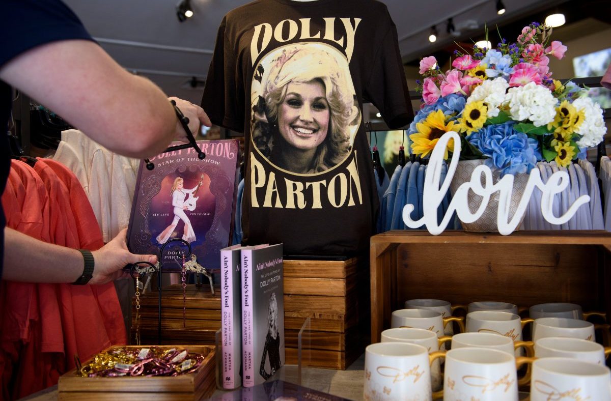 Dollywood gift shop with Dolly Parton t-shirt, books, mugs, and colorful floral display. A person browses merchandise.