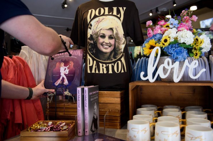 Dollywood gift shop with Dolly Parton t-shirt, books, mugs, and colorful floral display. A person browses merchandise.