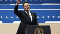 Elon Musk smiling and waving from a podium with the Seal of the President of the United States.