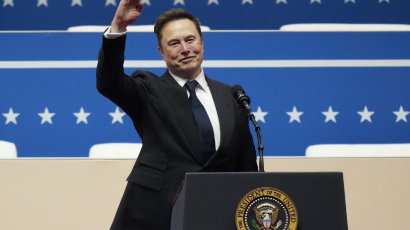 Elon Musk smiling and waving from a podium with the Seal of the President of the United States.
