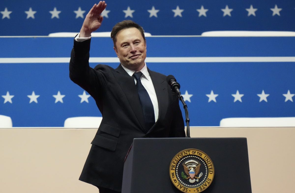 Elon Musk smiling and waving from a podium with the Seal of the President of the United States.
