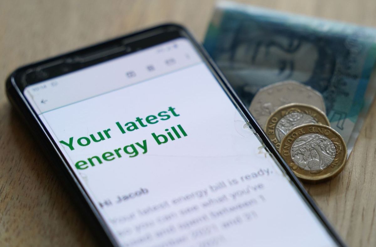 Smartphone displaying an energy bill notification with British coins and a banknote nearby.