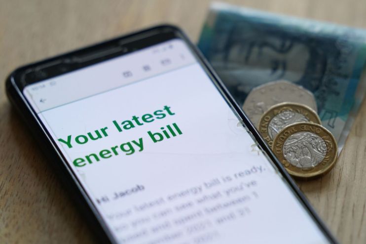 Smartphone displaying an energy bill notification with British coins and a banknote nearby.