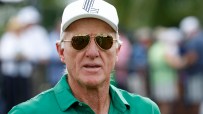 Greg Norman, CEO of LIV Golf, wearing a white cap, sunglasses, and a green polo shirt outdoors.