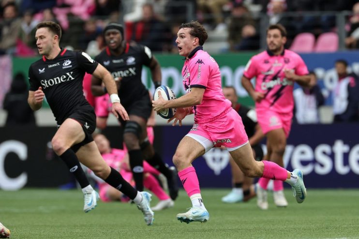 Rugby player in a pink uniform running with the ball, pursued by an opponent in a black jersey.