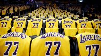 Rows of yellow Lakers jerseys with 77 on seats in a dark basketball arena.