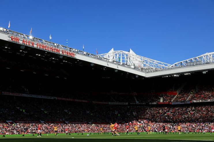 Football match in a stadium, Sir Alex Ferguson Stand visible on the roof, with fans and players on the field.