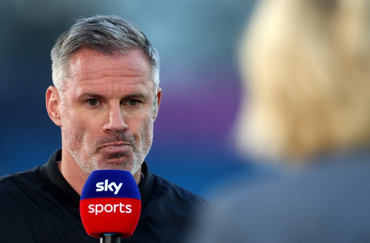 Jamie Carragher speaking into a Sky Sports microphone during an interview, with a blurred background.