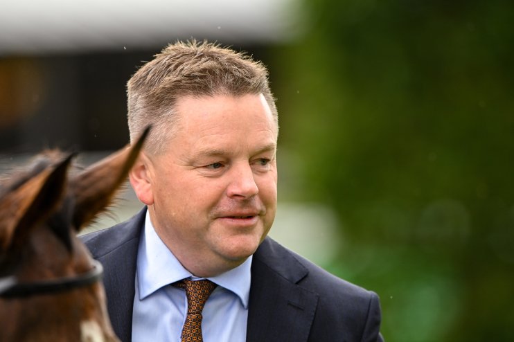 A man in a suit and patterned tie, with a horses ear visible, looks left against a green blurred background.