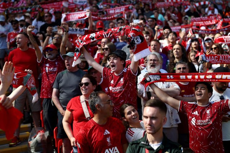 Liverpool FC fans cheering in a stadium, holding up red scarves and wearing team jerseys.