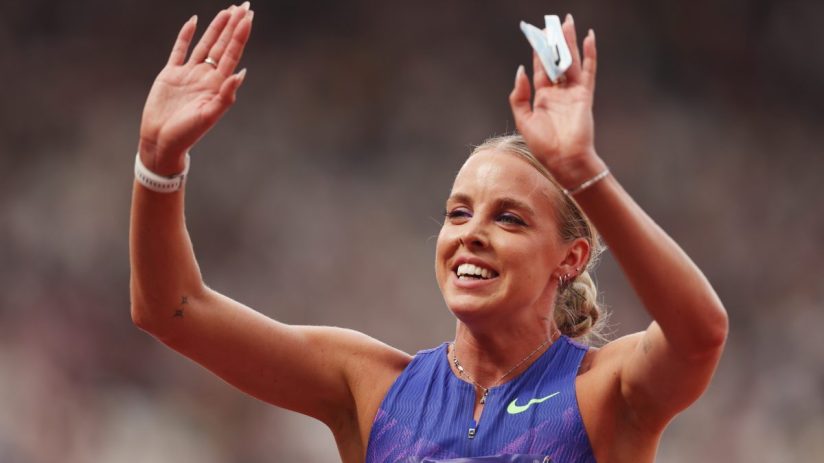 Keely Hodgkinson waves to the crowd at a track and field event, wearing a purple and black athletic top.