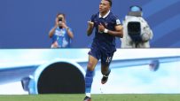 Kylian Mbapp&eacute; in a blue France soccer jersey with number 10, celebrating a goal on a green field.