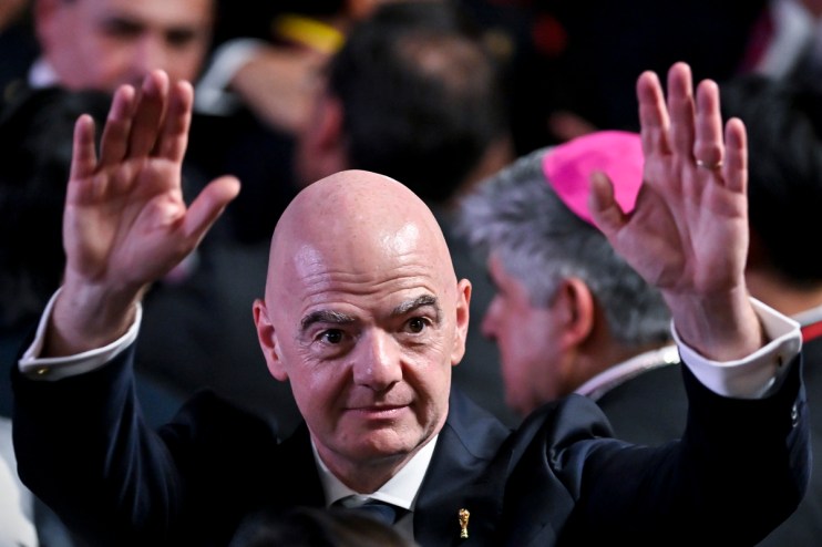 FIFA President Gianni Infantino with raised hands, wearing a dark suit and white shirt, at a public event.