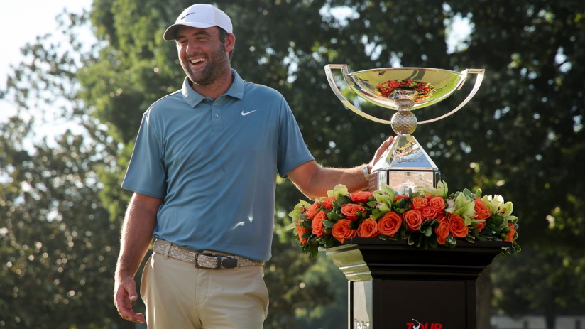 Scottie Scheffler, PGA Tour golfer, smiling next to the Tour Championship trophy with orange roses.