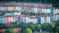 Aerial view of colorful residential houses built on a hillside, nestled among green trees, representing housing markets