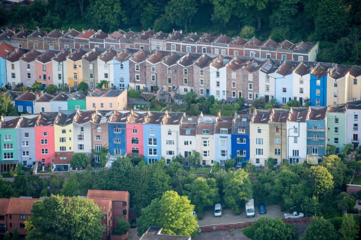 Aerial view of colorful residential houses built on a hillside, nestled among green trees, representing housing markets