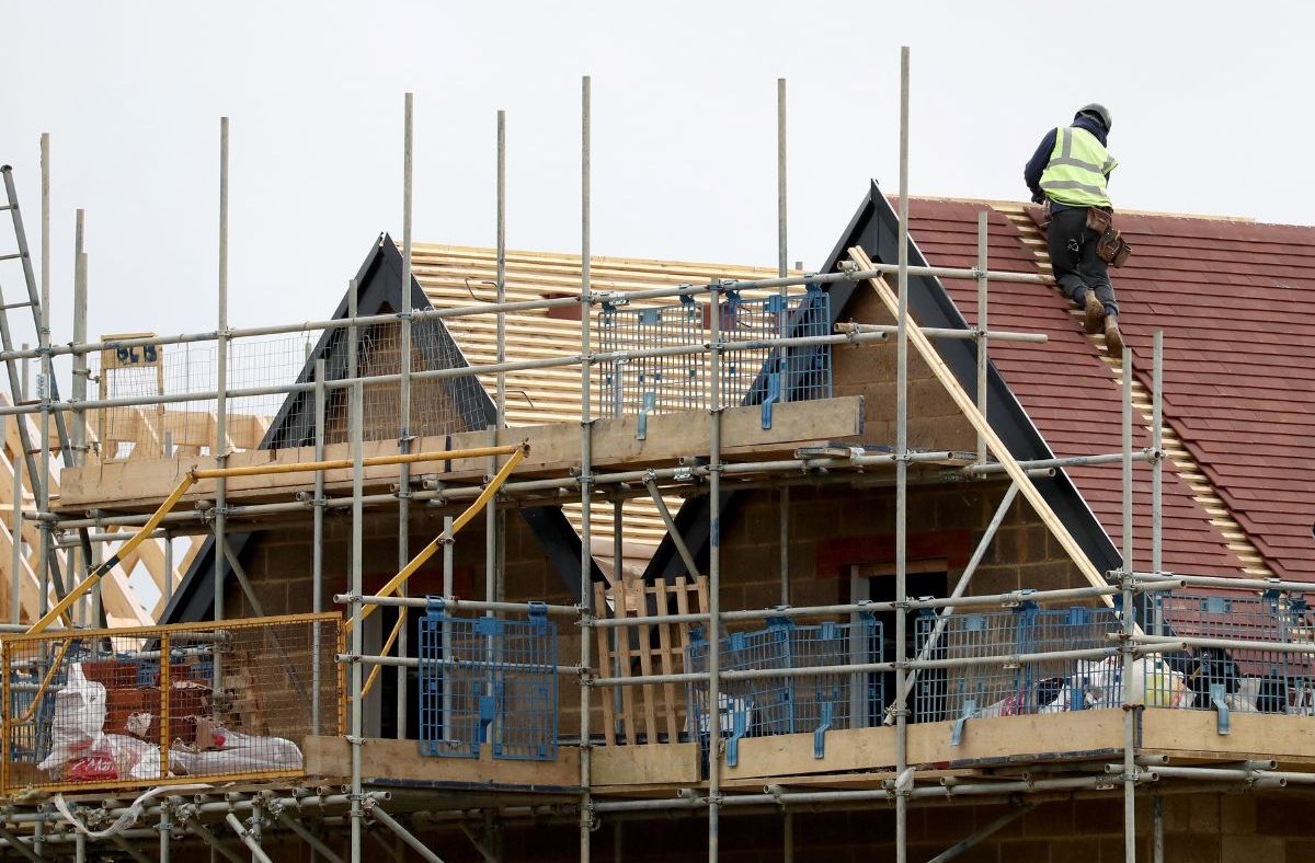 Construction worker on a new house roof, surrounded by scaffolding and building materials, illustrating housebuilding.