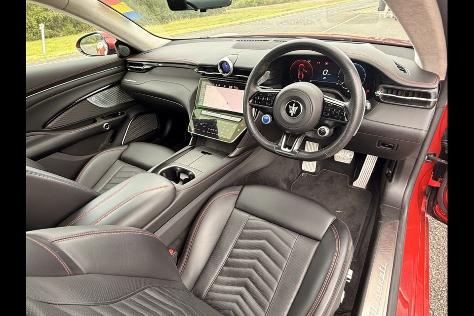 Interior of a red Maserati luxury car, showing the black leather seats with red stitching, dashboard, and steering wheel.