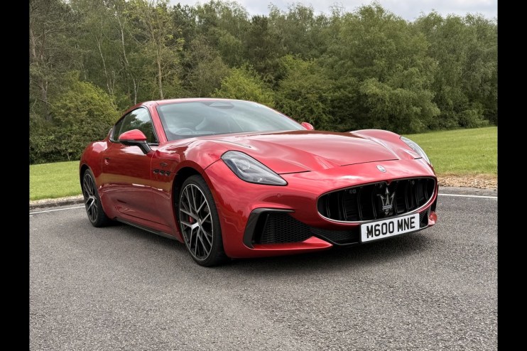 Red Maserati sports car parked on asphalt with trees and grass in the background.