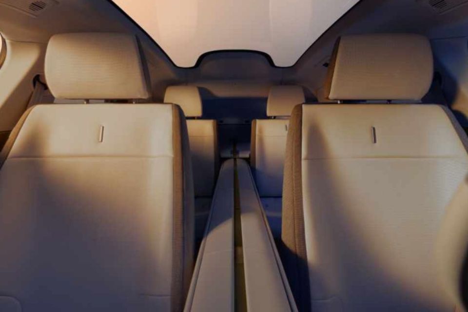 Modern Jaguar electric vehicle interior with beige seats and panoramic roof, looking back from front cabin