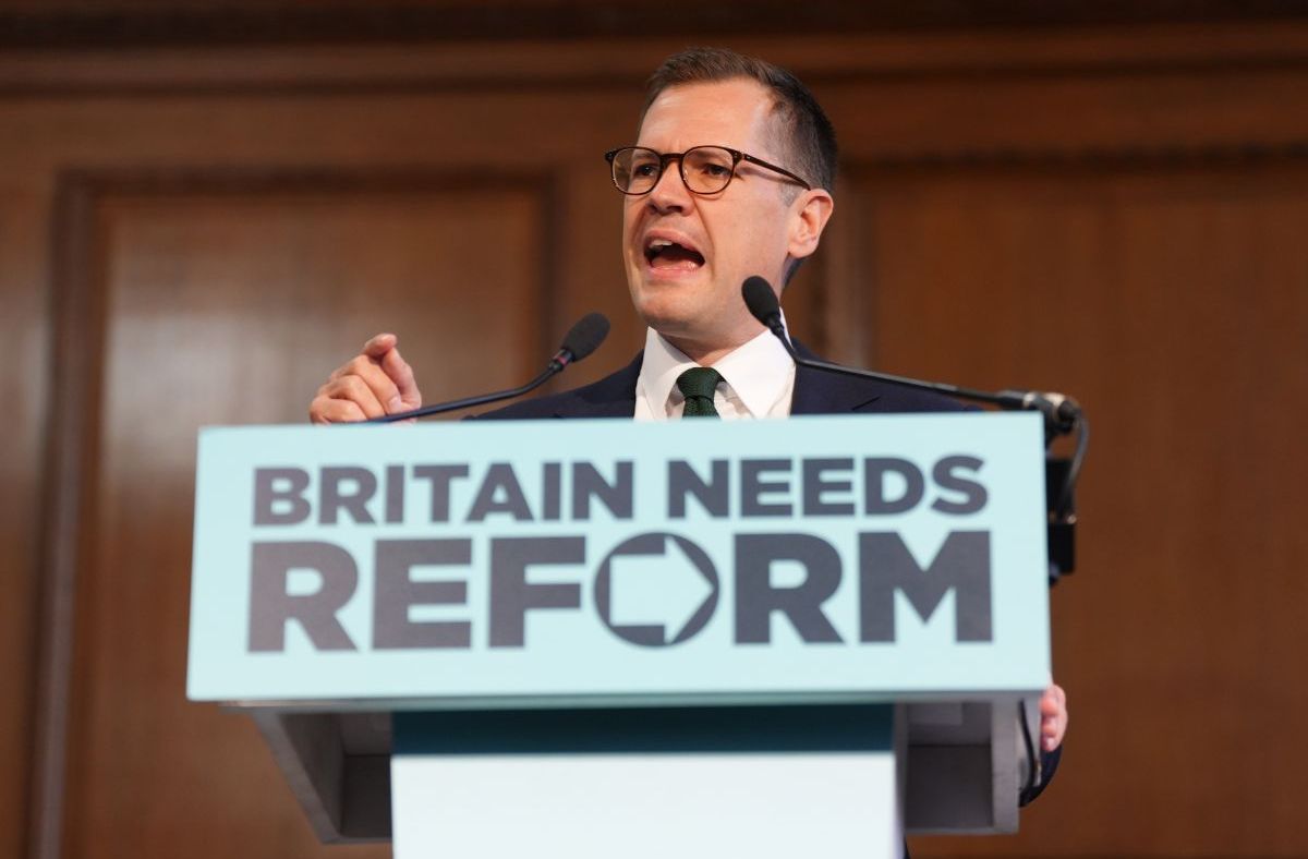 Robert Jenrick speaking at a podium with BRITAIN NEEDS REFORM sign, delivering a speech.
