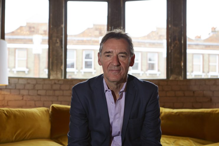 Jim ONeill, economist and former Goldman Sachs chairman, sitting on a yellow sofa in front of large windows.
