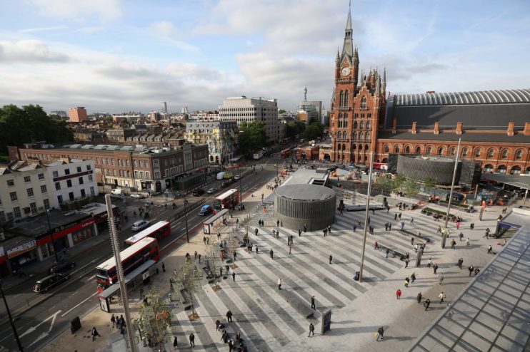 Aerial view of Kings Cross St. Pancras station and square, London, with people, buses, and surrounding buildings.
