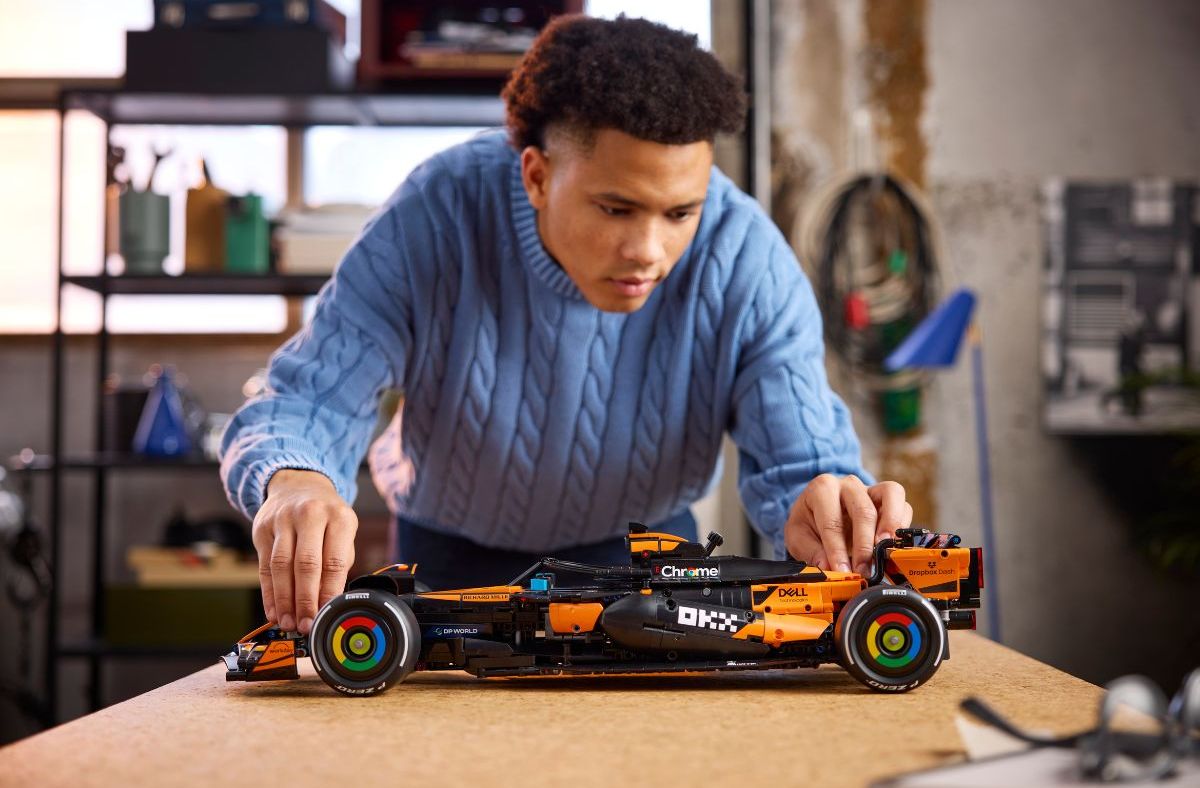 Young man in a blue sweater assembling a black and orange Lego McLaren Formula 1 race car model