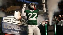 NFL player in green #22 jersey with arms raised, emerging through smoke onto the field at NFL London Games.